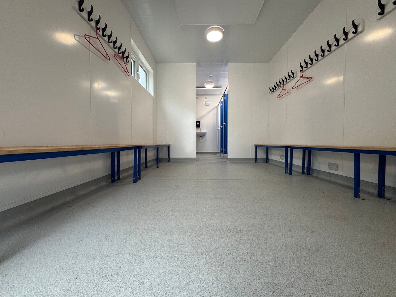Completed modular changing room with bench seating and coat hooks on both sides, blue doors and sanitary accommodation beyond
