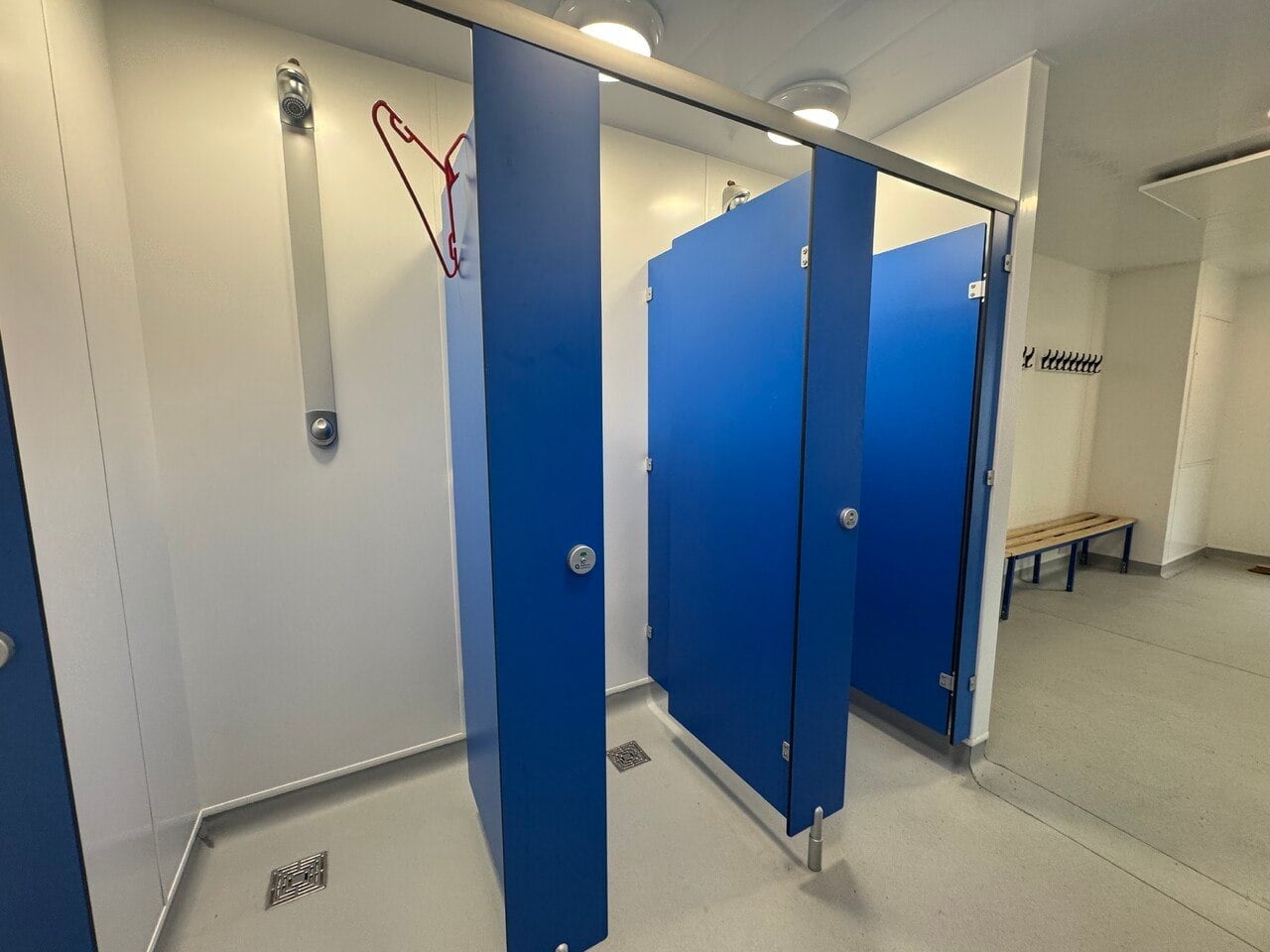 Completed shower and wet area with blue privacy cubicles, wall-mounted showers and floor drains