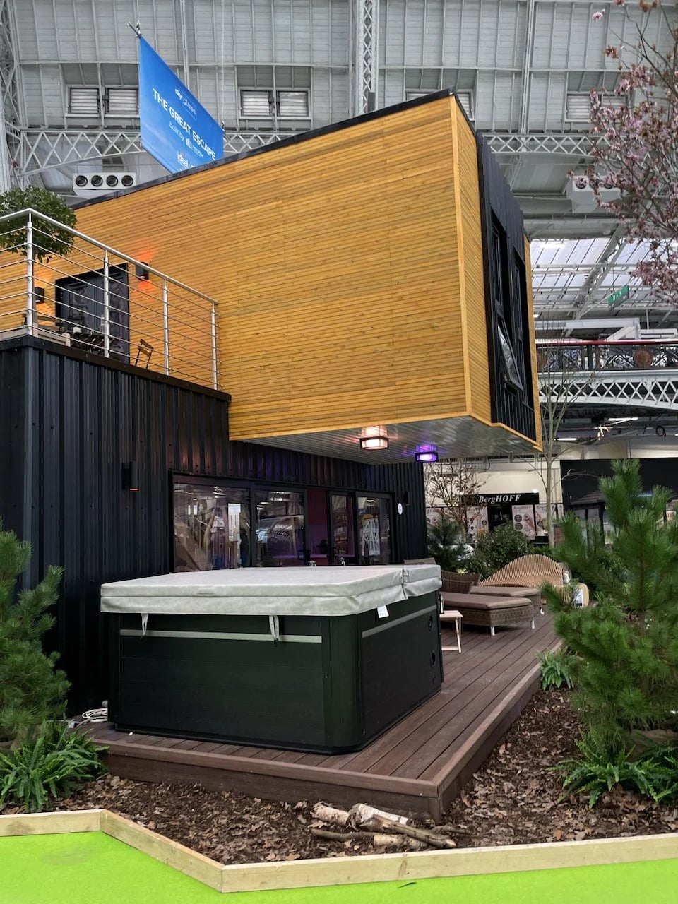 Timber-clad upper storey cantilevering over the dark ground floor of the exhibition build, with wall lights beneath