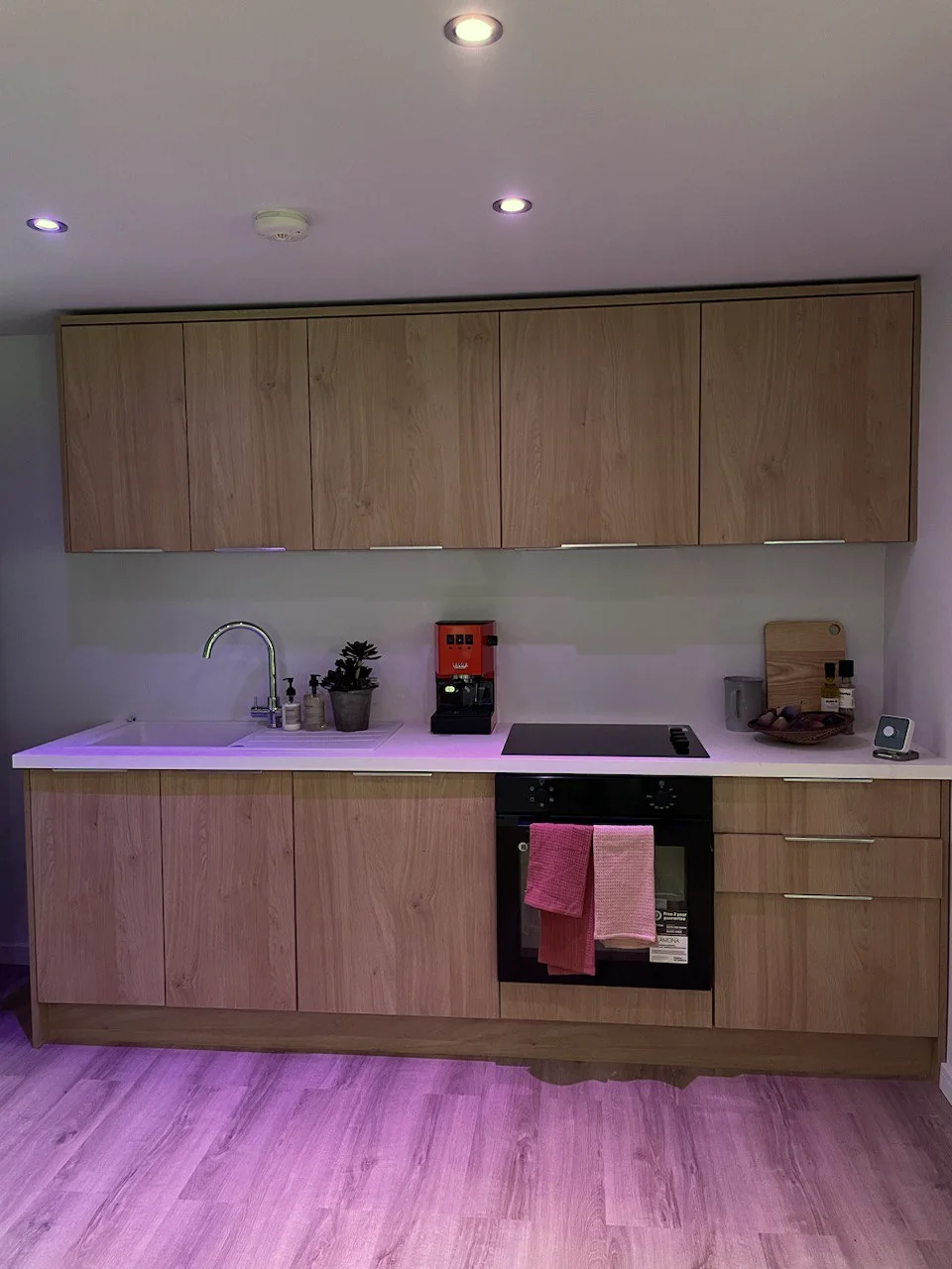 Fitted kitchen run with oak-effect units, integrated oven and hob under the exhibition lighting