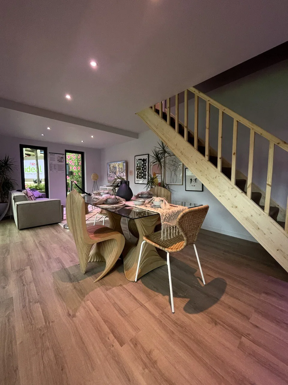 Open-plan living and dining space in the exhibition build, with the dining table, sofa and the timber stair to the first floor