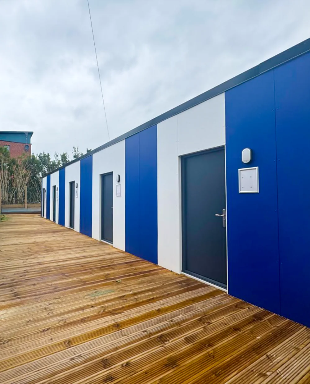Completed Sheffield Wednesday academy changing facility: white and blue panelled elevation with entrance doors along a timber-decked walkway